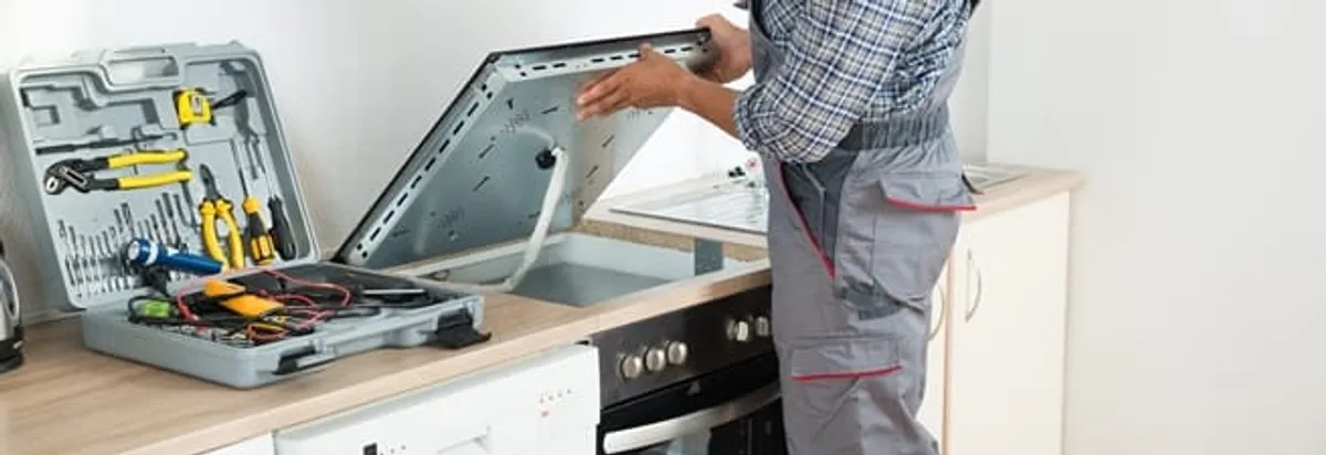 Cooktop repair technician lifting a built-in stovetop for service in Birmingham, AL