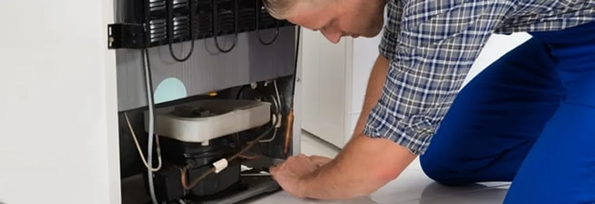 Refrigerator repair technician servicing the compressor and condenser area in Birmingham, AL