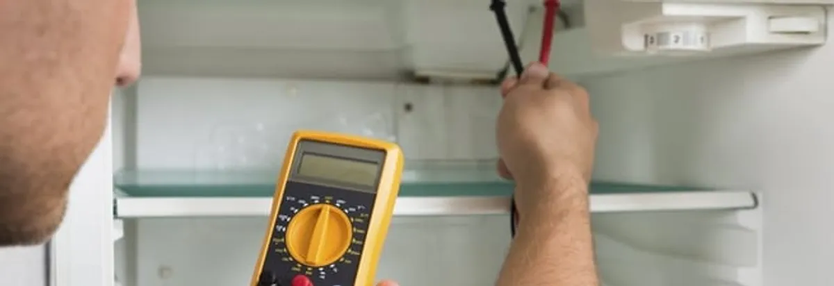 Refrigerator repair technician testing electrical components with a multimeter in Birmingham, AL