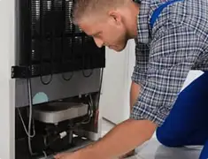 Refrigerator repair technician servicing the compressor and condenser area in Birmingham, AL
